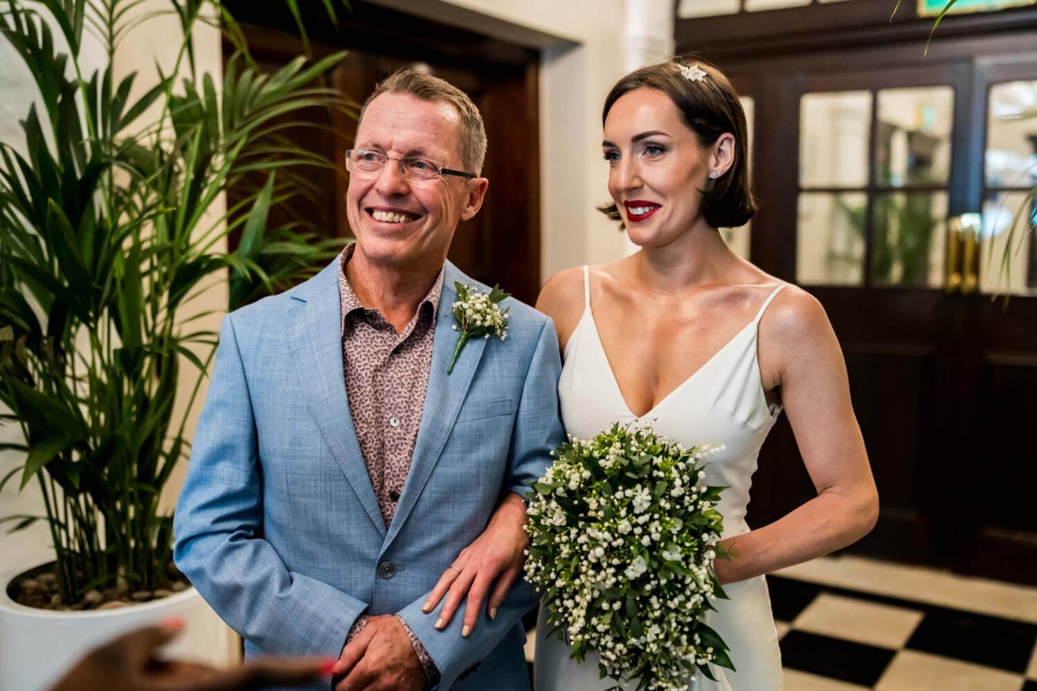 Father of bride and bride arm in arm smiling reading to walk in room Chelsea wedding.
