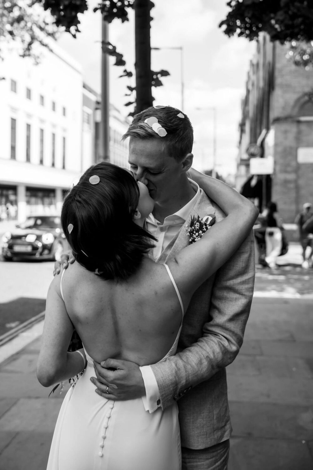 Bride and groom embracing a kiss after showered with confetti Chelsea wedding.