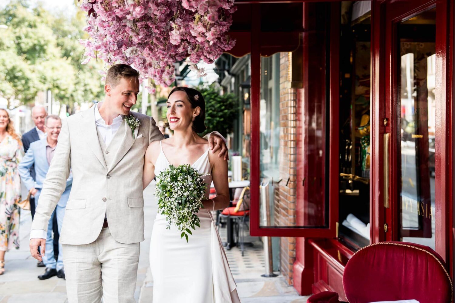 Bride and groom walking under pink flowers by restaurant Chelsea wedding.
