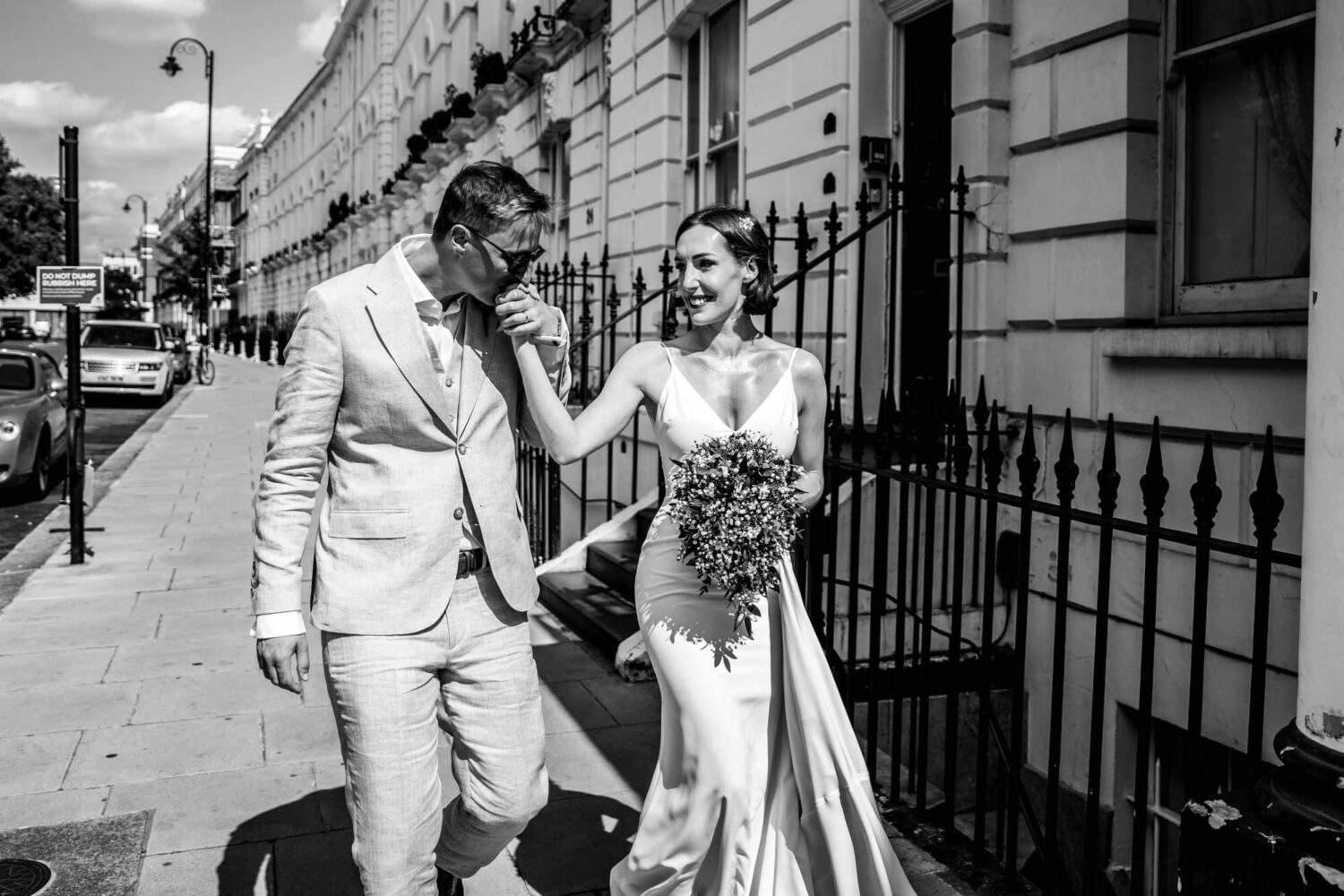 Groom takes bride's hand for a kiss walking along Chelsea street Chelsea wedding.