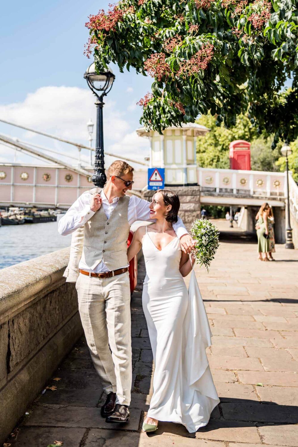 Bride and groom arm in arm walking along Thames riverbank Chelsea wedding.