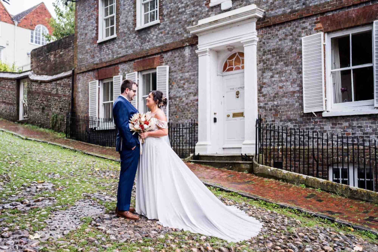 Bride and groom looking at each other on cobbled street and historic house on Keele street Lewes wedding.