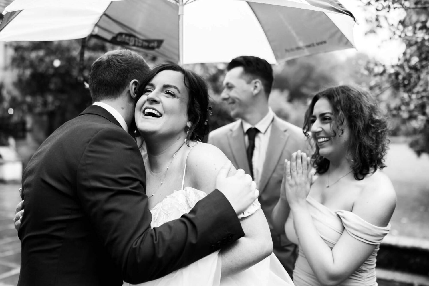 group of guests hugging bride with umbrella up Lewes wedding.