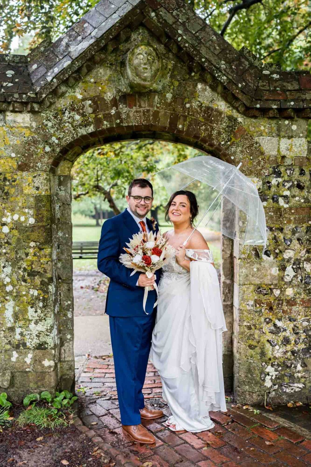 Bride and groom looking at the camera under pretty stone archway in southover grange gardens Lewes wedding.