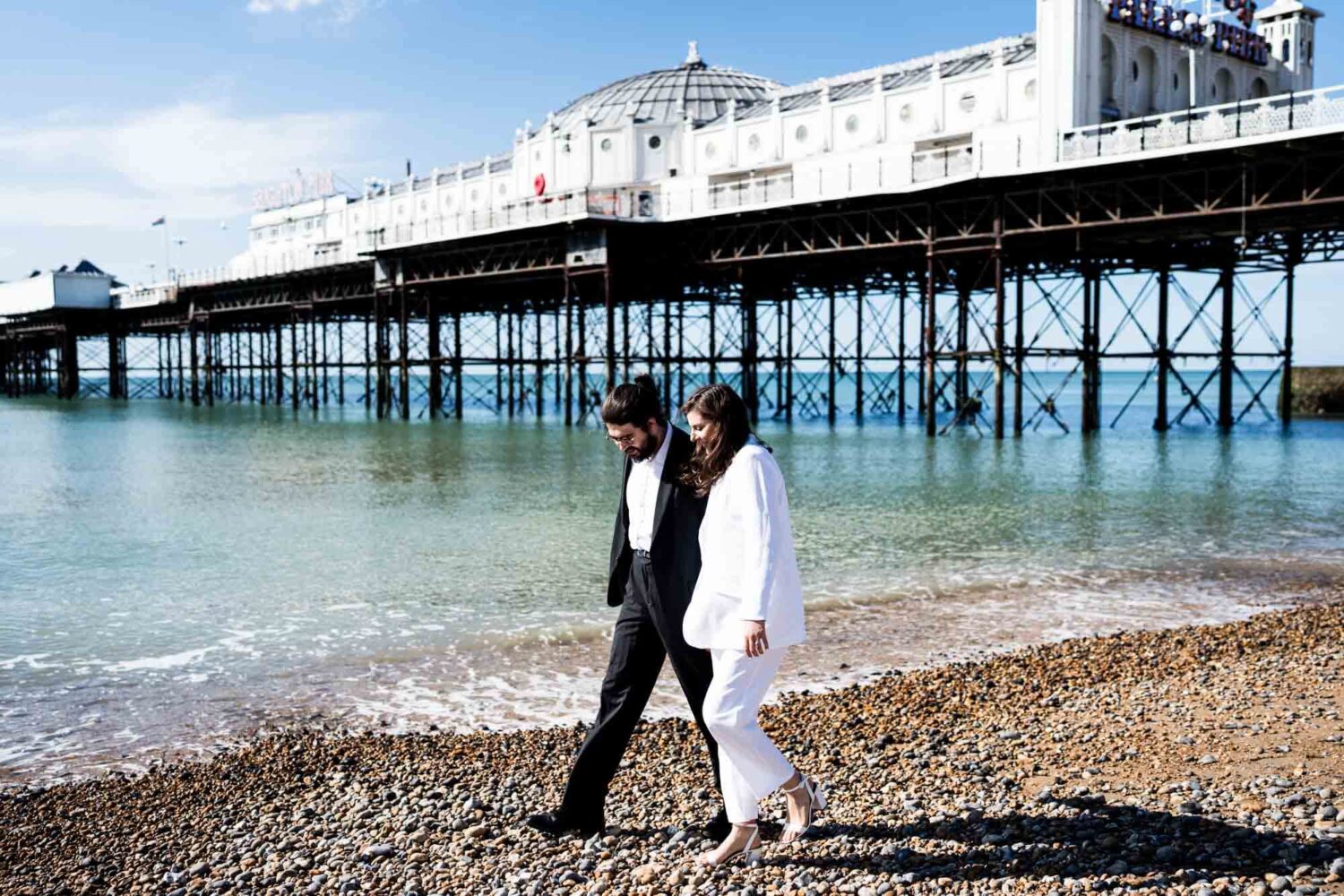 brighton pier in background couple walking along beach Brighton wedding.