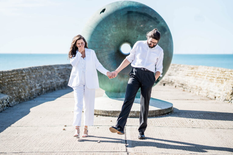 Walking along Brighton seafront couple holding handing laughing Brighton wedding.