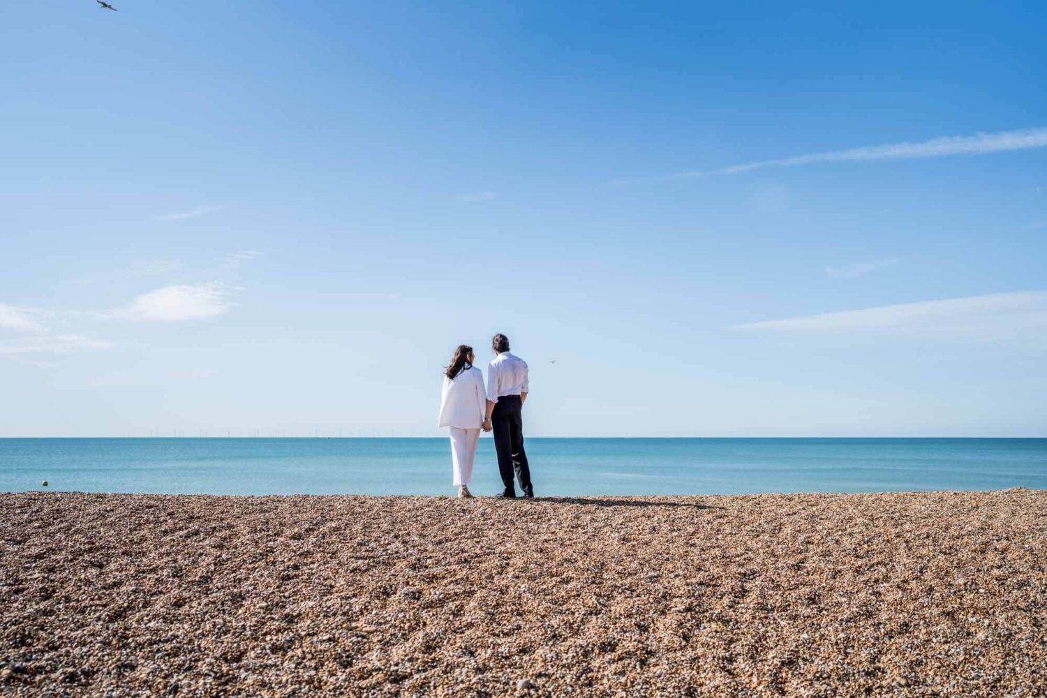 Couple standing with back to camera looking out to sea holding hands Brighton couple.