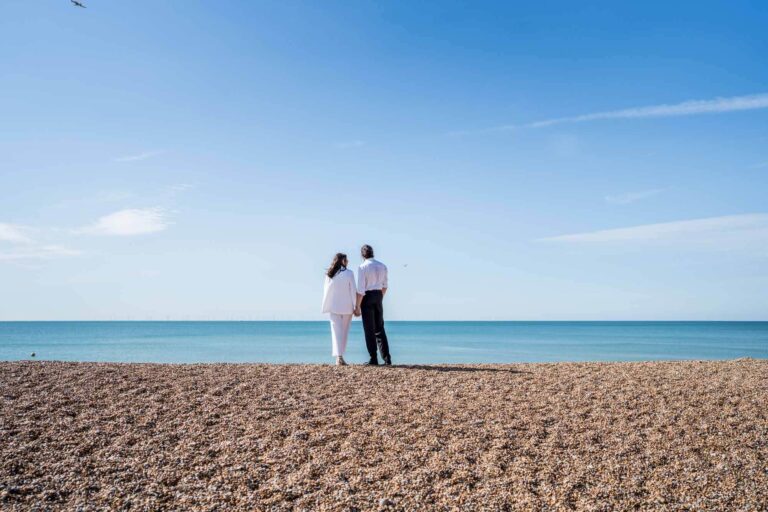 Couple standing with back to camera looking out to sea holding hands Brighton couple.