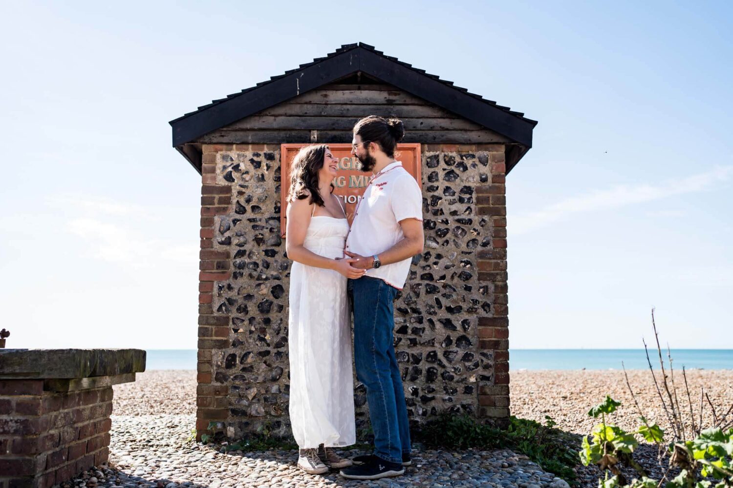 Male and female couple standing facing other with beach hut behind them Brighton wedding.