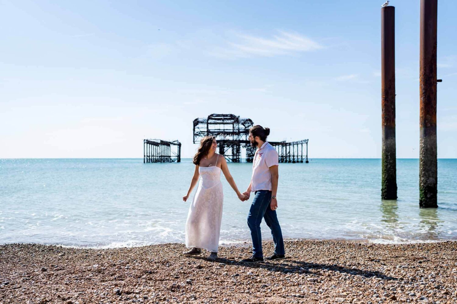 Bride leading the way walking along Brighton beach looking back towards partner Brighton wedding.
