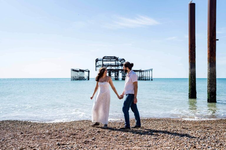 Bride leading the way walking along Brighton beach looking back towards partner Brighton wedding.