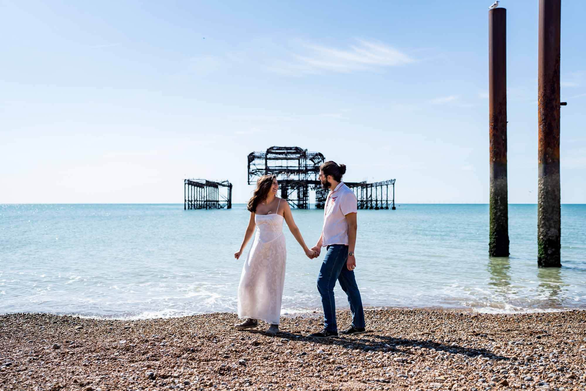 Bride leading the way walking along Brighton beach looking back towards partner Brighton wedding.